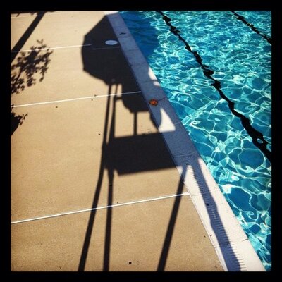 Pool reflected in sunlight with shadow of life guard chair.